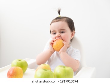 Baby Girl In Baby Chair Eating Apples On White Background. Baby First Solid Food