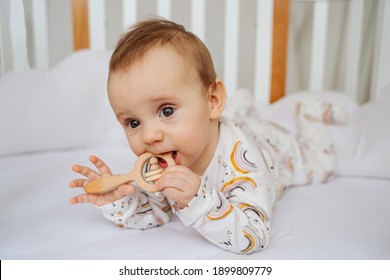 Baby girl chewing wooden teething toy lying  in cradle in baby's room.