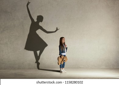 Baby girl dreaming about dancing ballet. Childhood and dream concept. Conceptual image with shadow of ballerina on the studio wall - Shutterstock ID 1158280102