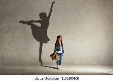 Baby girl dreaming about dancing ballet. Childhood and dream concept. Conceptual image with shadow of ballerina on the studio wall - Shutterstock ID 1158280108
