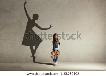 Baby girl dreaming about dancing ballet. Childhood and dream concept. Conceptual image with shadow of ballerina on the studio wall
