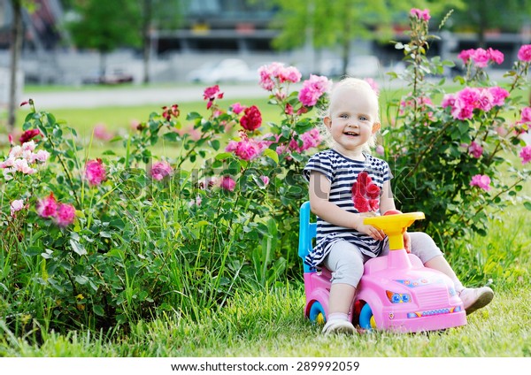 baby\
girl driving pink toy car on a background of\
roses