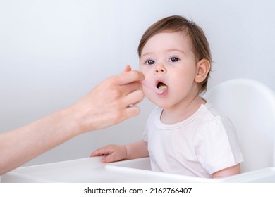 Baby girl eating blend mashed food sitting, on high chair, mother feeding child, hand with spoon for vegetable lunch, baby weaning, first solid food for young kid. - Shutterstock ID 2162766407