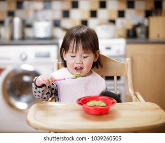 Baby Girl Eating  Mashed Avocado At Home Kitchen