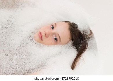 Baby Girl Face In Bathtub Among Soap Suds And Bubbles. Child Bathing