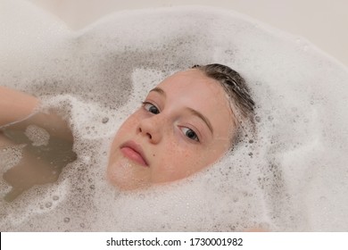 Baby Girl Face With Freckles In Bathtub Among Soap Suds And Bubbles. Child Bathing