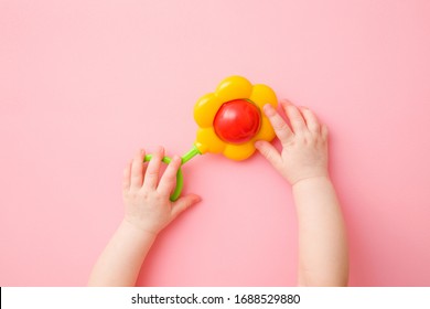 Baby Girl Hands Playing With Colorful Flower Rattle On Light Pink Floor Background. Pastel Color. Closeup. Toys Of Development For Infant.