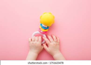 Las manos de una niña que juega con el colorido rattle en el fondo del suelo rosa claro. Color pastel. Cerrando. Juguetes de desarrollo para el niño. Captura de punto de vista.