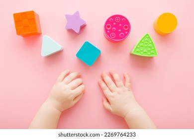 Baby girl hands playing with colorful plastic shapes on light pink table background. Pastel color. Closeup. Infant development toys. Point of view shot.