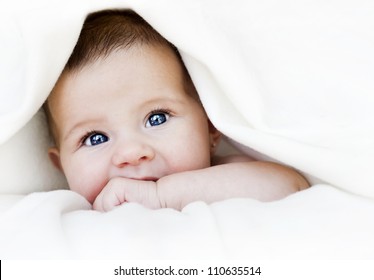 baby girl is hiding under the white blanket