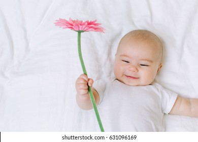 Baby girl holding a flower on her bed