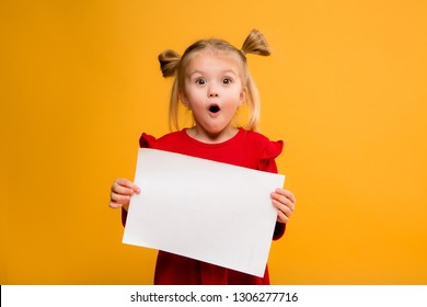 baby girl holding white sheet.Cute little girl with white sheet of paper.yellow background.copy spase.Little girl holding empty sheet of a paper