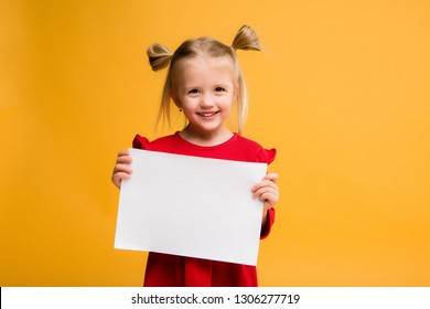 baby girl holding white sheet.Cute little girl with white sheet of paper.yellow background.copy spase.Little girl holding empty sheet of a paper