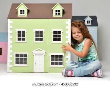 Baby Girl Kid Playing With Doll House Sitting On A Floor In Play Room At Home Or Kindergarten With Closed Eyes Listening And Waiting For Surprise