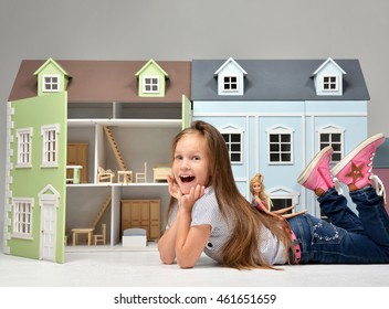 Baby Girl Kid playing with doll house stuffed with mini furniture toys and doll lying on a floor in play room at home or kindergarten