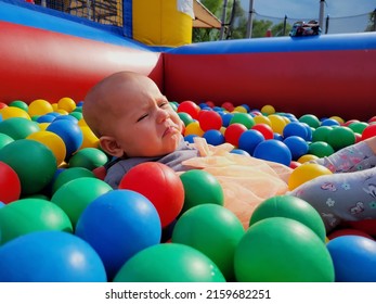 Baby Girl Lying Down In Colourful Balls And Reaching Hand To Go Out