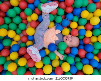 Baby Girl Lying Down In Colourful Balls And Reaching Hand To Go Out