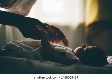 Baby Girl Lying On The Bad. Mother Standing Near The Bed. Silhouette Of Mother And Baby. Concept Photo Parenthood And Motherhood.