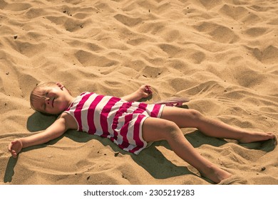 Baby girl lying on sand. Adorable kid sunbathing at summertime. - Powered by Shutterstock