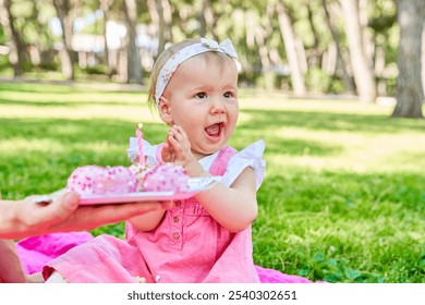 Baby girl in a pink dress clapping with excitement while celebrating her birthday with pink cake pops in a park. - Powered by Shutterstock