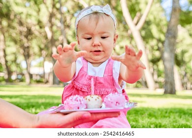 Baby girl in a pink dress clapping with excitement while celebrating her birthday with pink cake pops in a park. - Powered by Shutterstock