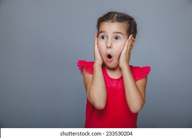 baby girl in red dress put her hands on the face of surprise on a gray background