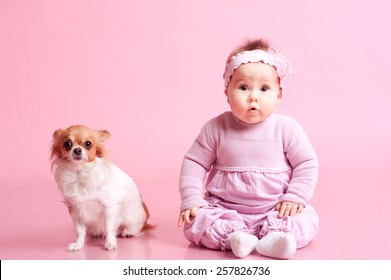 Baby girl sitting on floor with little dog over pink. Wearing stylish clothes. Looking at camera. Childhood.