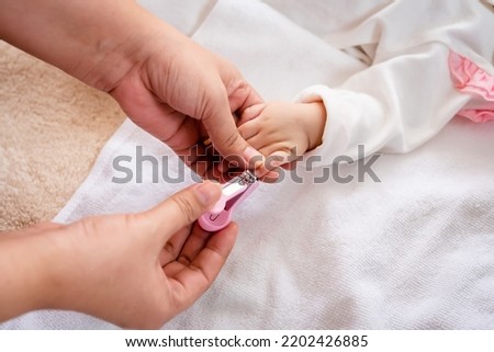 A baby girl sleeps on a brown bed, comfortably, Mother took the time of the baby to sleep, brought clippers to cut the nails of the sleeping baby, carefully, so that the baby does not feel.