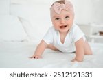 A baby girl is smiling at home on a white bed with a bow on her head, a happy healthy child of six months is laughing.