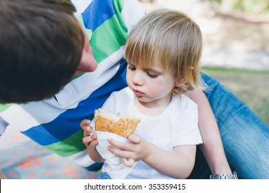 Baby Girl Toddler Eating A Sandwich Outdoors In The Park Lying Near Her Father