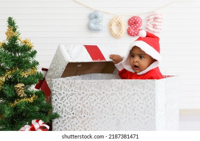 Baby Girl Toddler Sitting In A Large Gift Box White Background With Christmas Tree And Doll Cute Little Girl Dressed For Christmas Holiday Concept Celebrate With Family Happy New Year. Tim Christmas