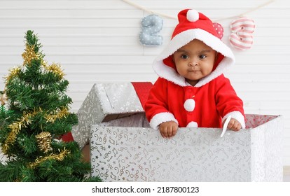 Baby Girl Toddler Sitting In A Large Gift Box White Background With Christmas Tree And Doll Cute Little Girl Dressed For Christmas Holiday Concept Celebrate With Family Happy New Year. Tim Christmas