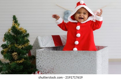 Baby Girl Toddler Sitting In A Large Gift Box White Background With Christmas Tree And Doll Cute Little Girl Dressed For Christmas Holiday Concept Celebrate With Family Happy New Year. Tim Christmas