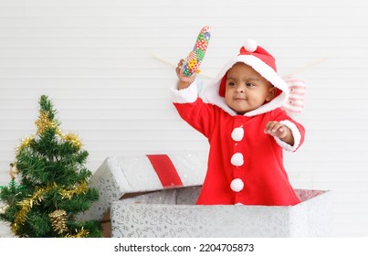 Baby Girl Toddler Sitting In A Large Gift Box White Background With Christmas Tree And Doll Cute Little Girl Dressed For Christmas Holiday Concept Celebrate With Family Happy New Year. Tim Christmas