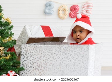 Baby Girl Toddler Sitting In A Large Gift Box White Background With Christmas Tree And Doll Cute Little Girl Dressed For Christmas Holiday Concept Celebrate With Family Happy New Year. Tim Christmas