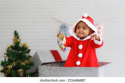 Baby Girl Toddler Sitting In A Large Gift Box White Background With Christmas Tree And Doll Cute Little Girl Dressed For Christmas Holiday Concept Celebrate With Family Happy New Year. Tim Christmas