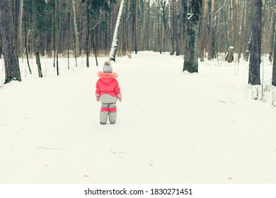 baby girl walking on a snowy road in the park in winter.
