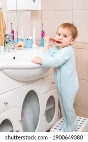 Baby Girl Wearing Blue Blanket Sleeper Learning To Brush Teeth In A Bathroom