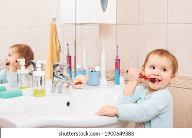 Baby Girl Wearing Blue Blanket Sleeper Learning To Brush Teeth In A Bathroom