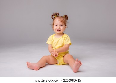 baby girl with yellow bodysuit sitting on a white background - Shutterstock ID 2256980715