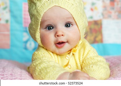 Baby Girl In Yellow Knit Hooded Sweater In Front Of Quilt