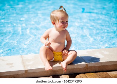 baby girl in yellow swimming diapers sitting by the pool in summer