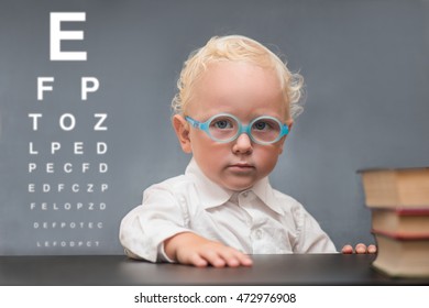 Baby With Glasses Sits At A Table On The Background Of The Table For An Eye Examination