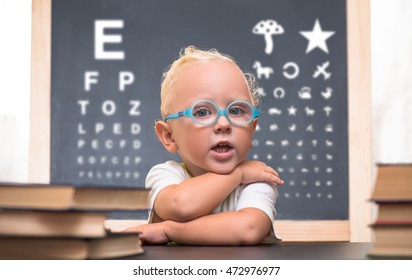 Baby with glasses sits at a table on the background of the table for an eye examination