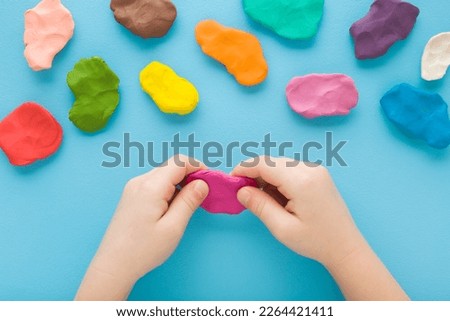 Baby hands holding and kneading modeling clay on light blue table background. Pastel color. Closeup. Point of view shot. Toddler development. Preparing material for making different colorful shapes.