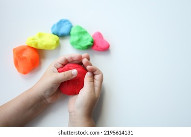 Baby hands holding and kneading red modeling clay on white table background. Closeup. Toddler development. Preparing material for making different colorful shapes. - Powered by Shutterstock