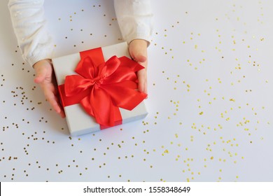 Baby hands holding present with red bow on light background with gold sparkles. Christmas, New Year. Flat lay. Festive backdrop - Shutterstock ID 1558348649