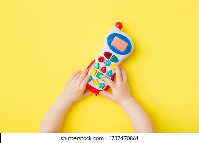 Baby Hands Playing With Colorful Toy Of Mobile Phone On Bright Yellow Table Background. Closeup. Point Of View Shot.