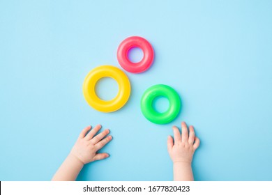 Baby hands playing with green, yellow and pink plastic rings on light blue table background. Pastel color. Closeup. Toys of development for little kids.