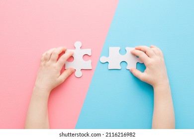 Baby hands playing and putting together white puzzle pieces on light blue pink table background. Pastel color. Closeup. Point of view shot. Children development. Two color sides.